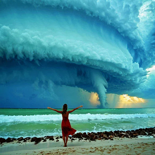 Digital artwork of a woman in a red dress stands on a beach with her arms outstretched, facing an approaching storm with massive, swirling clouds. 